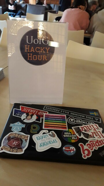 Hacky Hour logo on display stand, and laptop covered in stickers